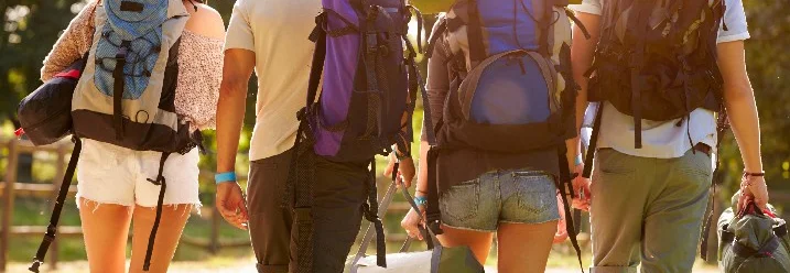 Vier Personen mit Rucksäcken gehen auf einem Feld.
